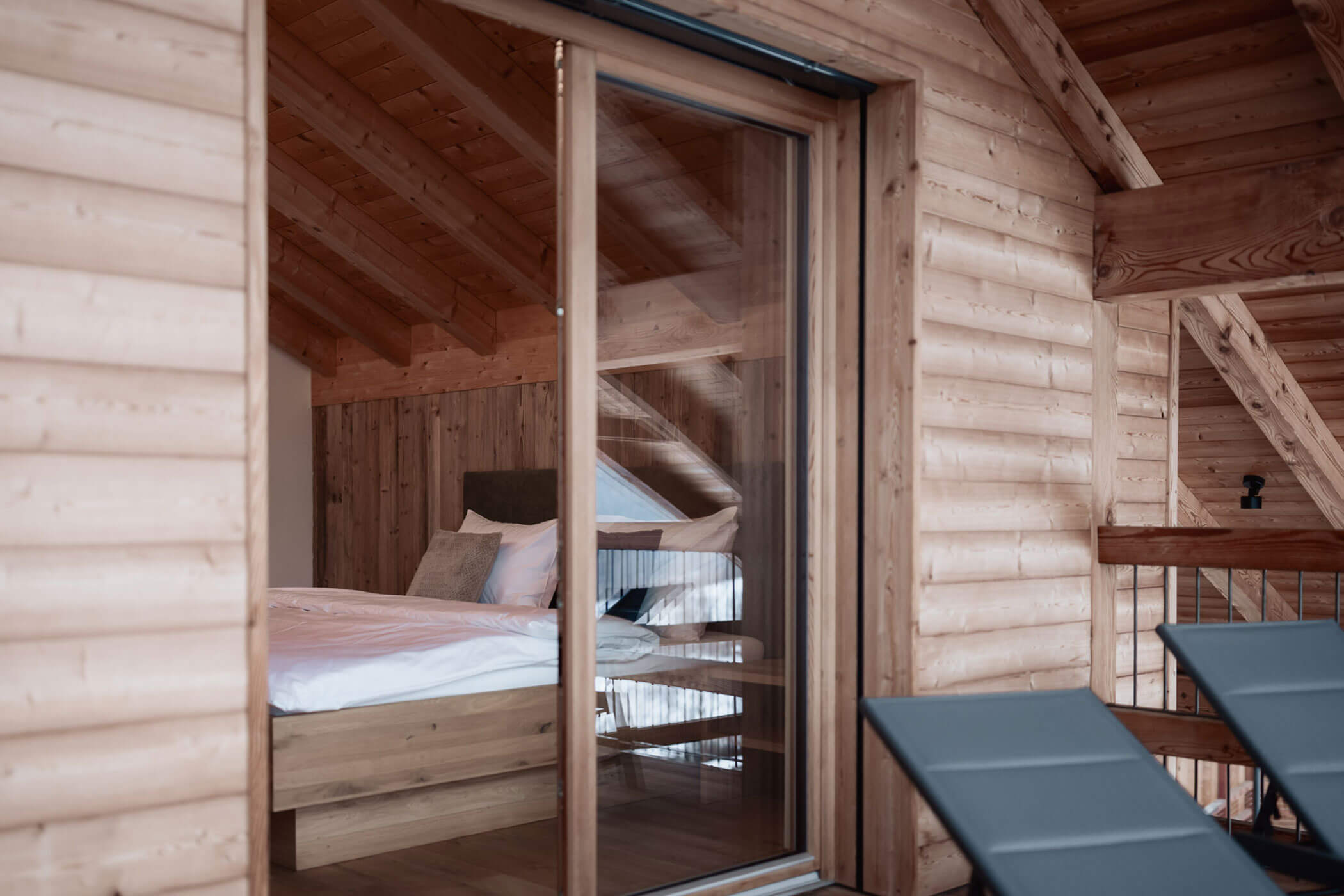 Ein gemütliches Schlafzimmer im Loft-Stil mit einem ordentlich gemachten Bett, gesehen durch eine Glasschiebetür. - Lantl Deluxe Apartments