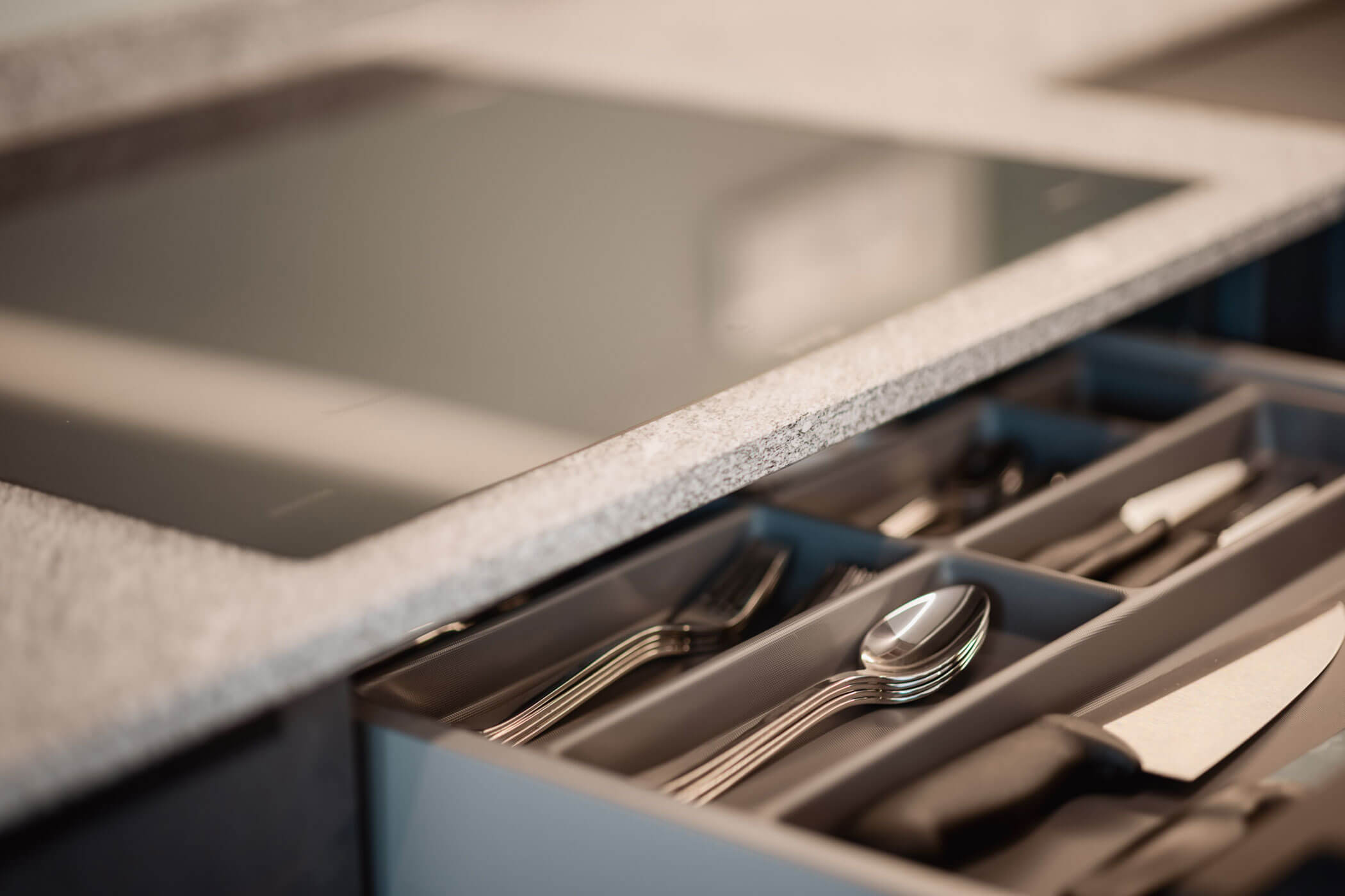 Offene Küchenschublade mit ordentlich sortiertem Besteck und Messern unter einer Arbeitsplatte und einem Kochfeld. - Lantl Deluxe Apartments