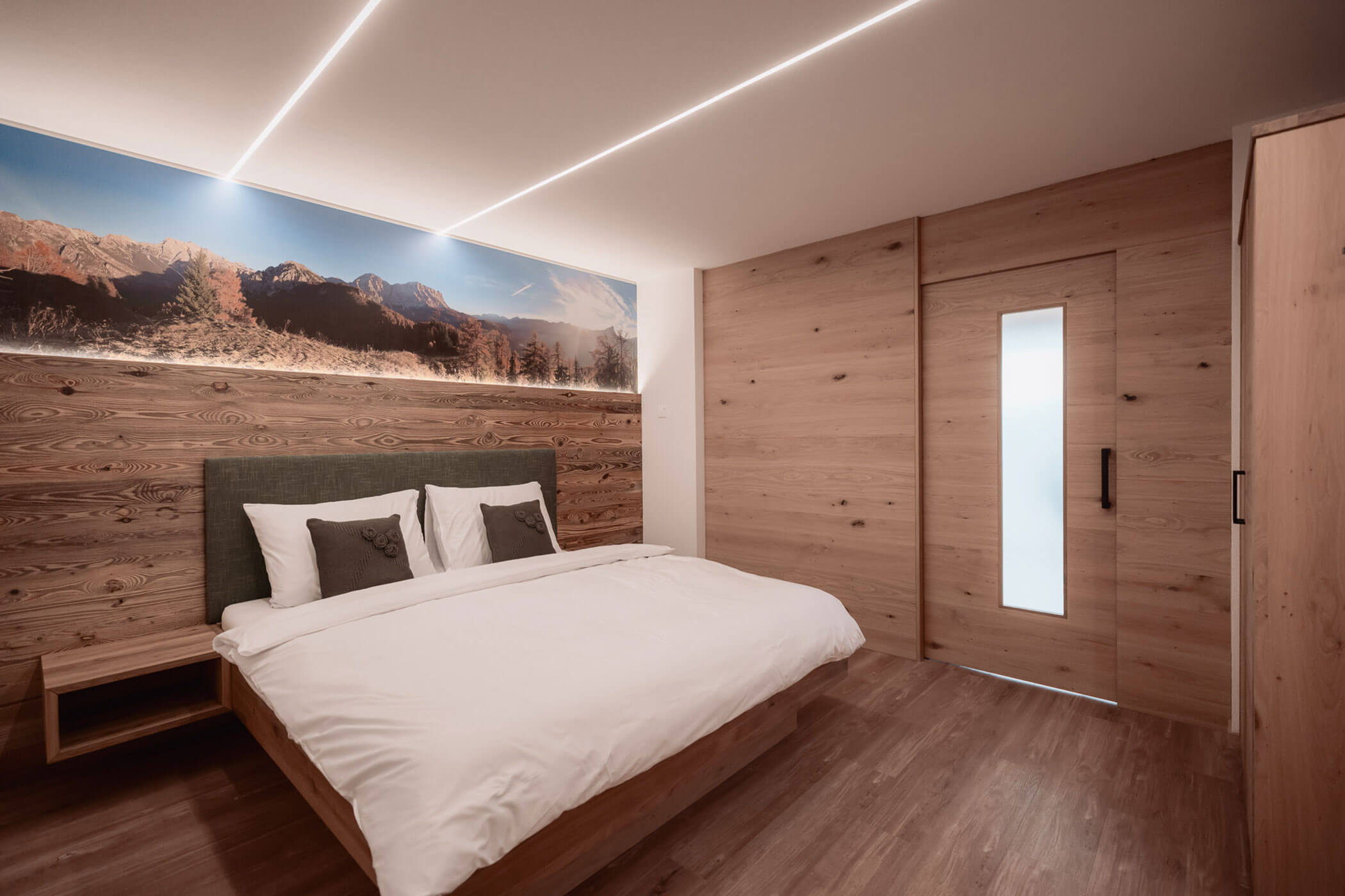 Minimalistisches Schlafzimmer mit Holzwänden, Doppelbett, Naturmotiven und sanfter Beleuchtung. - Lantl Deluxe Apartments