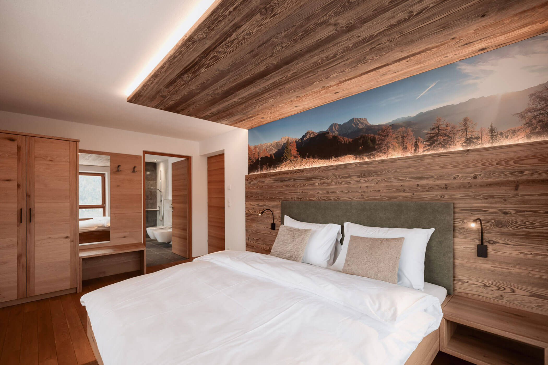 Modernes Schlafzimmer mit Holzdekor, großem Bett und einer Wandmalerei mit Berglandschaft über dem Kopfteil. - Lantl Deluxe Apartments