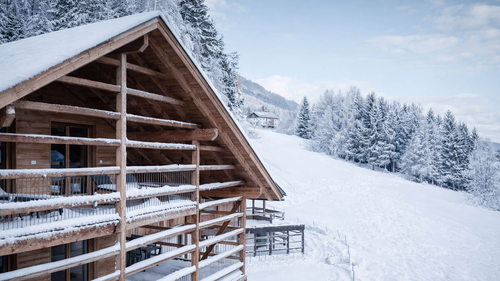 Ein Holzchalet in den verschneiten Bergen, im Hintergrund schneebedeckte Bäume und ein Hang. - Lantl Deluxe Apartments