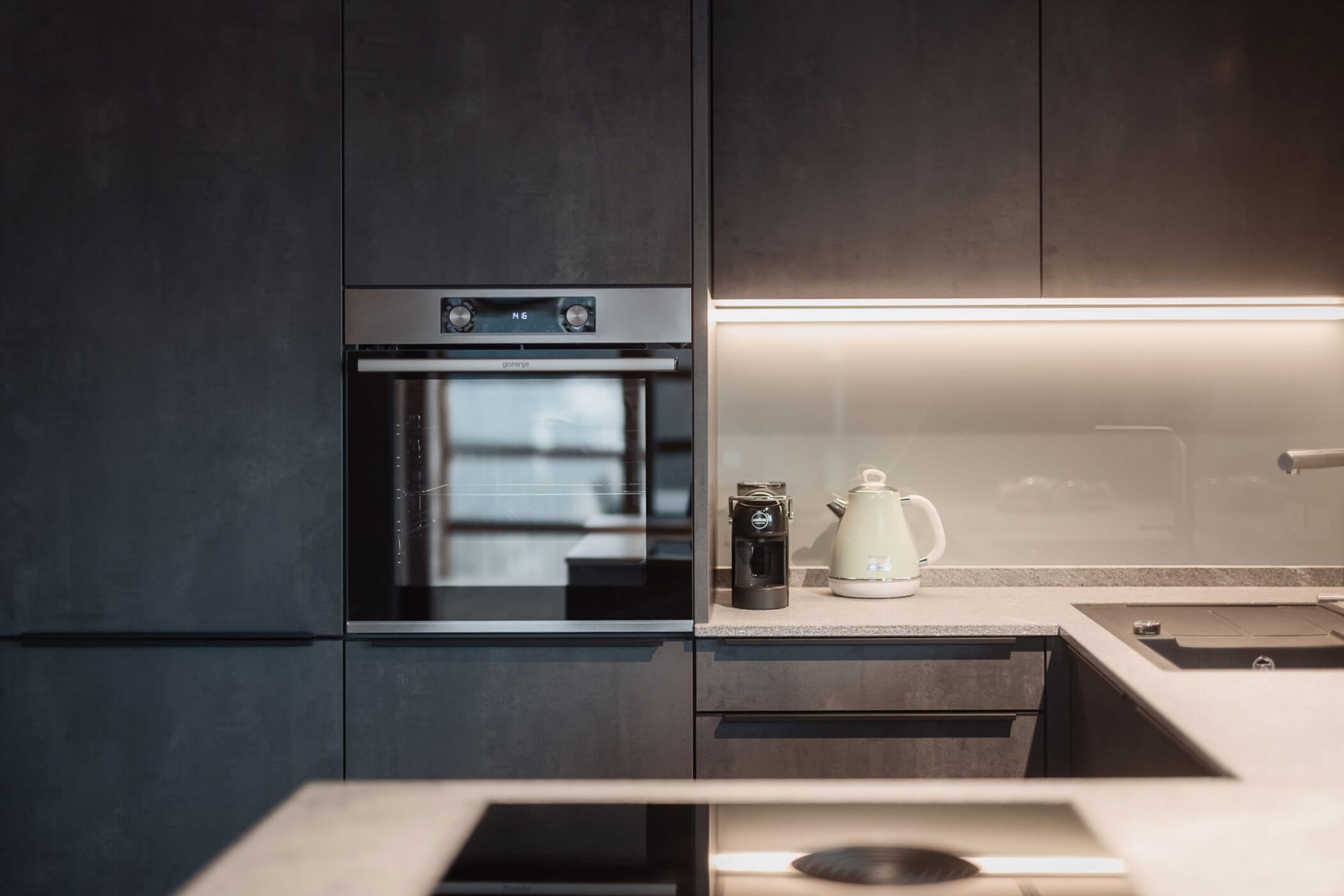 Moderne Küche mit Einbaubackofen, Kaffeemaschine, Wasserkocher und Unterbauleuchten. - Lantl Deluxe Apartments