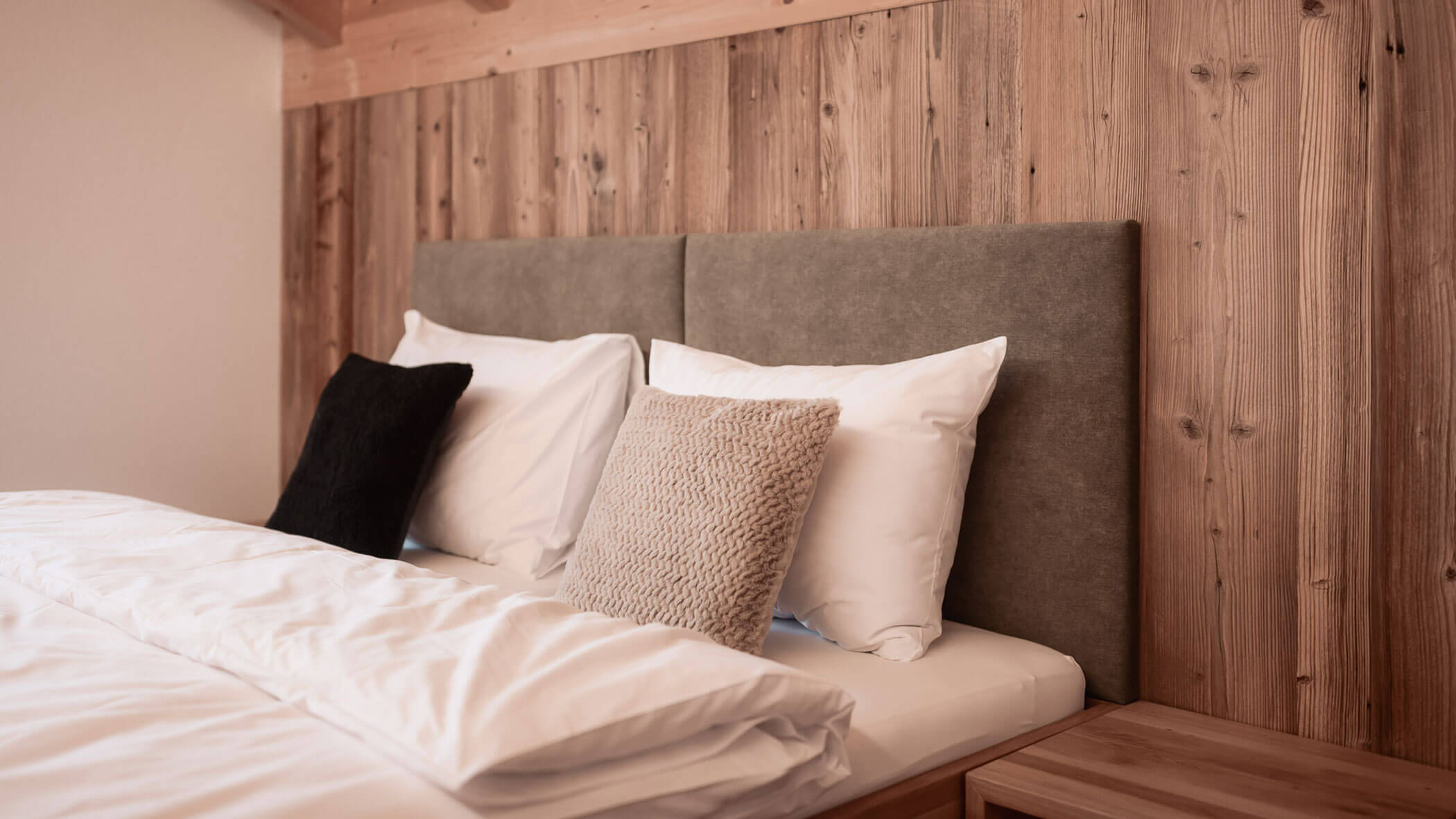 Ein ordentlich gemachtes Bett mit weißer Bettwäsche, drei Kissen und einem Kopfteil aus Holz in einem gemütlichen Zimmer. - Lantl Deluxe Apartments
