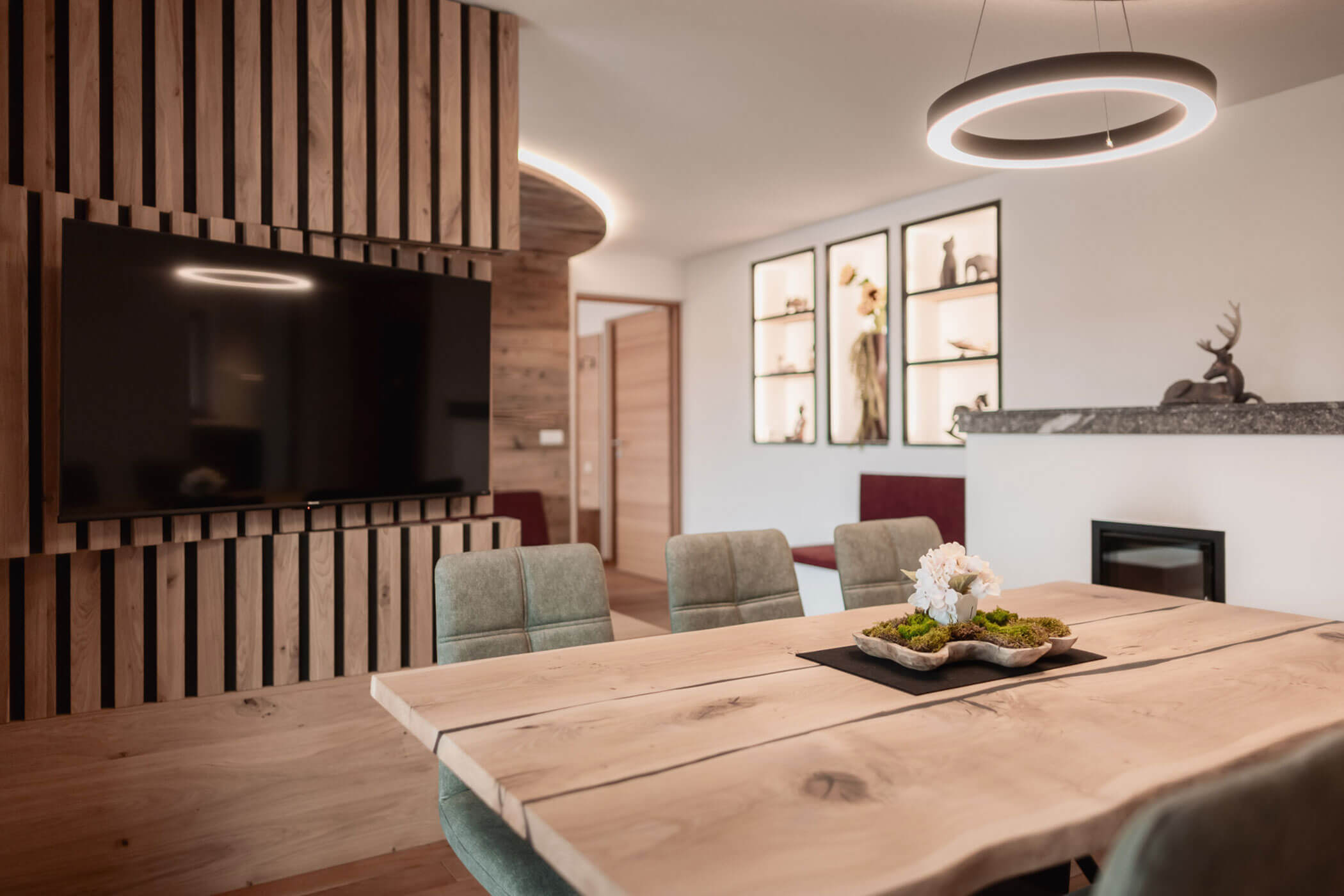 Moderner Essbereich mit einem Holztisch, grünen Stühlen, einem an der Wand montierten Fernseher und zeitgemäßer Einrichtung. - Lantl Deluxe Apartments