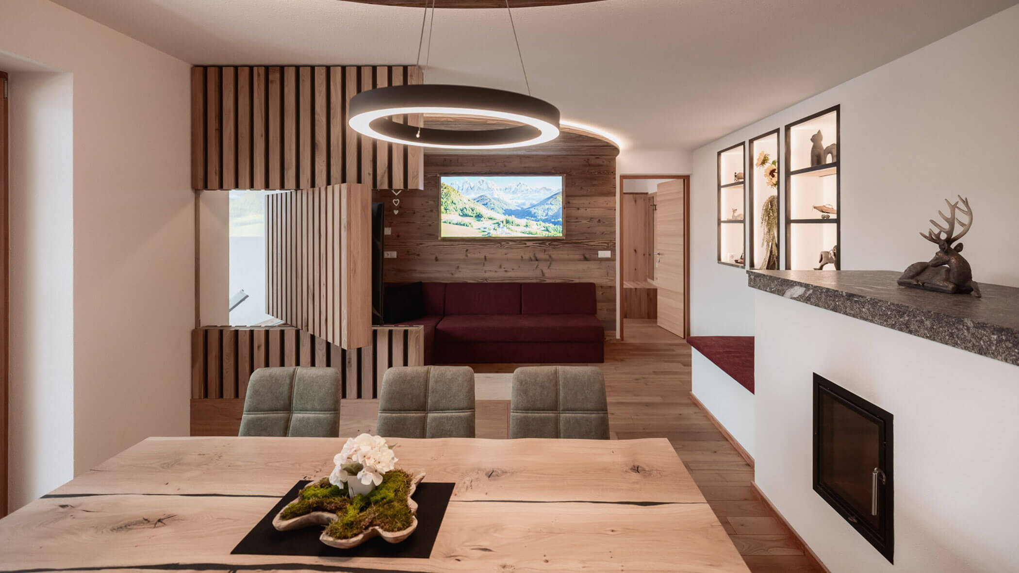 Moderner Wohn- und Essbereich mit Holzakzenten, grünen Stühlen, Wandbildern, einem Kamin und dekorativen Regalen. - Lantl Deluxe Apartments