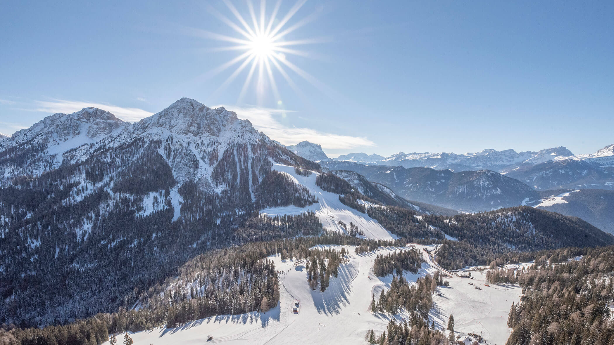 Schneebedeckte Berge und Kiefern unter strahlendem Sonnenschein vor einem strahlend blauen Himmel. - Lantl Deluxe Apartments