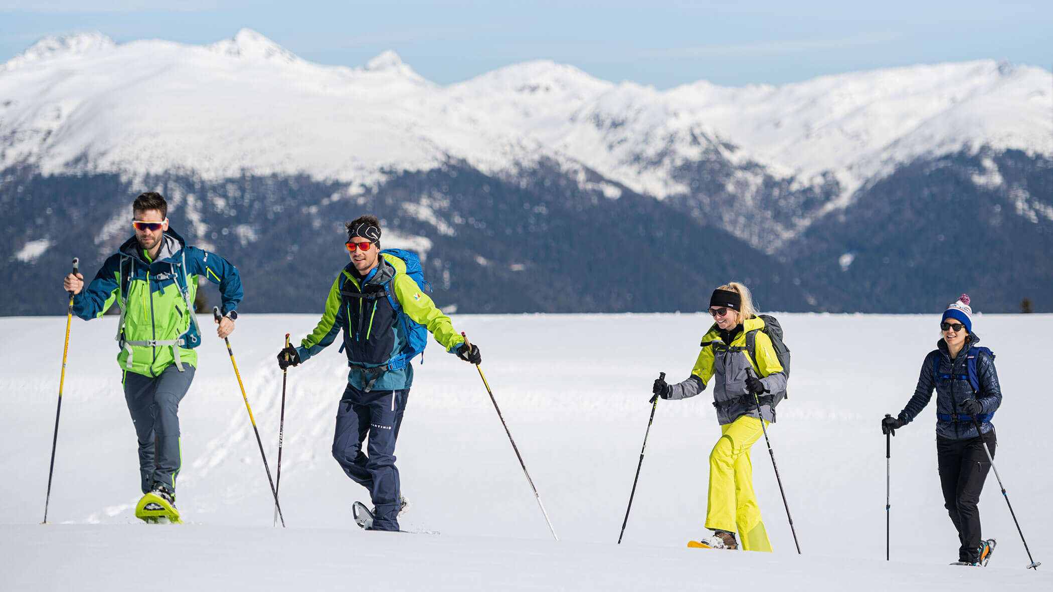 Vier Personen, die mit Wanderstöcken in den verschneiten Bergen wandern, in Winterkleidung, vor dem Hintergrund schneebedeckter Gipfel. - Lantl Deluxe Apartments